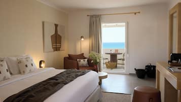 Habitación de hotel con cama, escritorio, silla, una mesita y vista al mar.