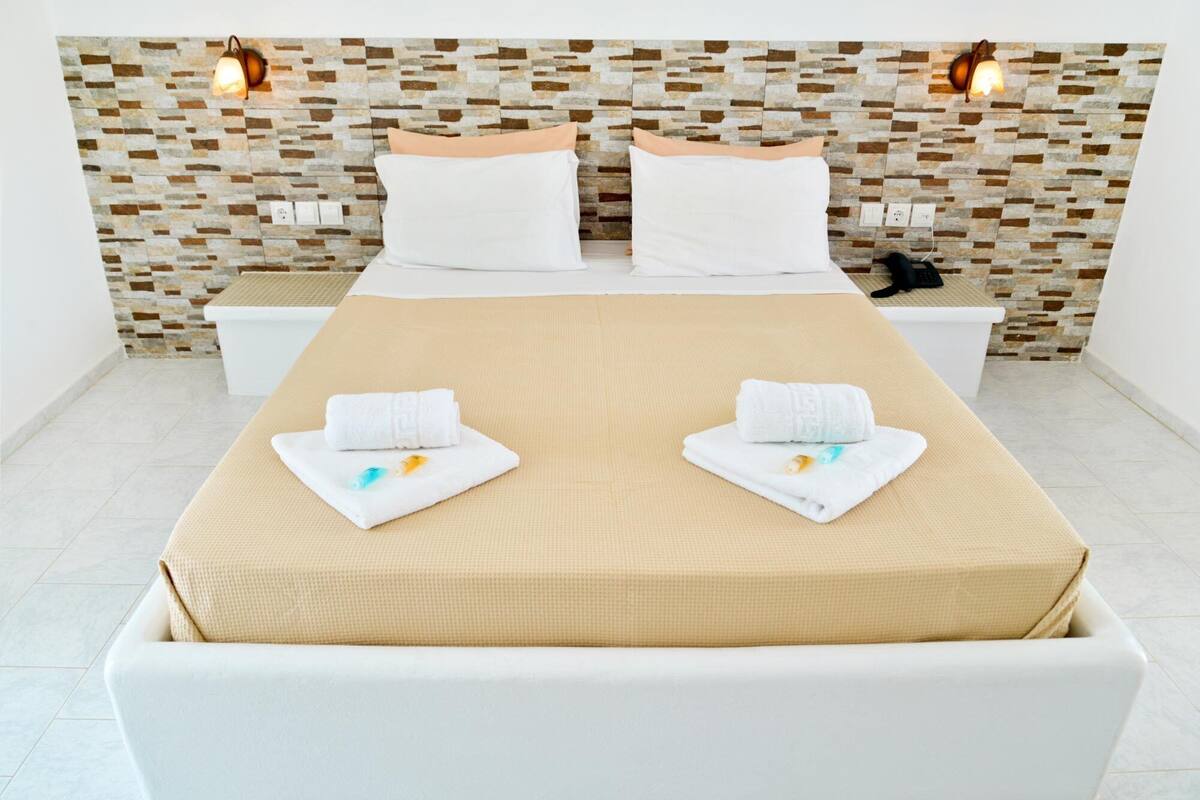 A neatly arranged hotel room with a bed, two bedside tables, and a headboard with a stone pattern.