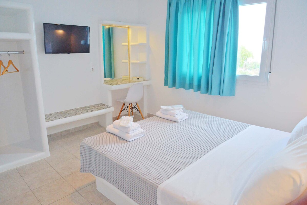 Una habitación de hotel con cama, un banco, un televisor y un ventanal con cortinas.
