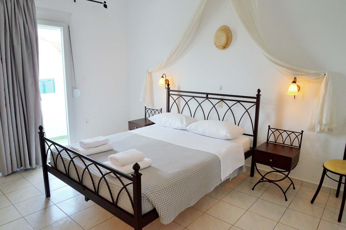 Un dormitorio con cama, mesitas de noche, una silla y una ventana con cortinas.