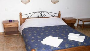 A bedroom with a wooden bed frame, a blue patterned bedspread, two bedside tables, and wall-mounted lamps. - Anezina (Milos)