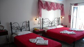 A hotel room with two beds, each with a red bedspread and white pillows. There are two bedside tables, one with a lamp and the other with a telephone. The room has a simple, clean design with white walls and a tiled floor. - Anezina (Milos)