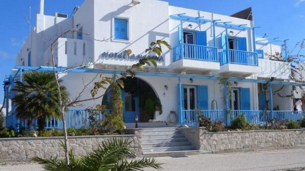 A two-story building with a white facade and blue accents, featuring a balcony and a staircase leading to the entrance. - Anezina (Milos)