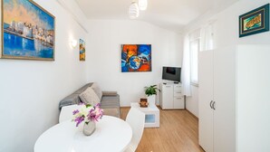 A modern living room with a sofa, a dining table with flowers, a TV, and artwork on the walls.