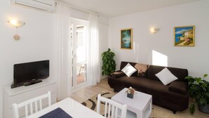 A living room with a brown sofa, white TV stand, and a dining area with a white table and chairs.