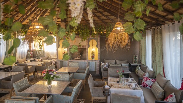 A restaurant with multiple seating areas, including tables and booths, with hanging plants and decorative lighting. - Riad Les Oliviers & Spa (Marrakech)