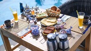 A table set with breakfast items including bread, pastries, and beverages near a pool. - Riad Les Oliviers & Spa (Marrakech)