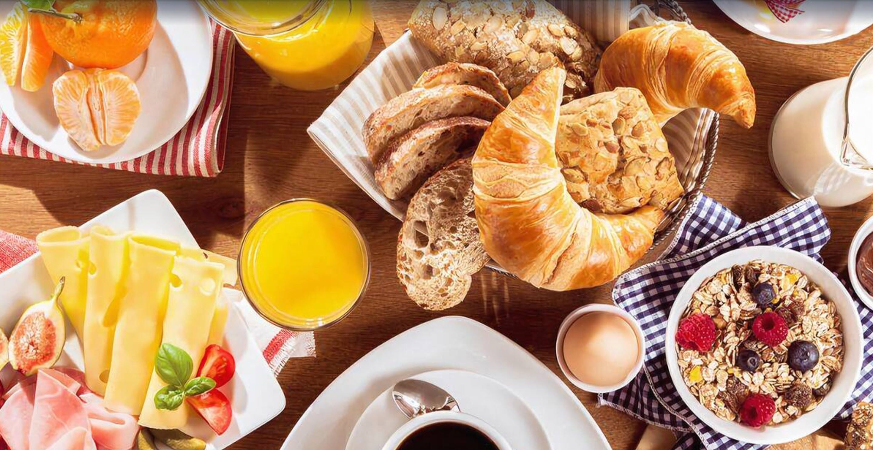 Una mesa de desayuno con cruasanes, rodajas de naranja, queso, pan y un tazón de cereal.