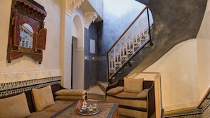 A room with a sofa, a patterned coffee table, and a staircase with ornate railings. - Riad Les Oliviers & Spa (Marrakech)