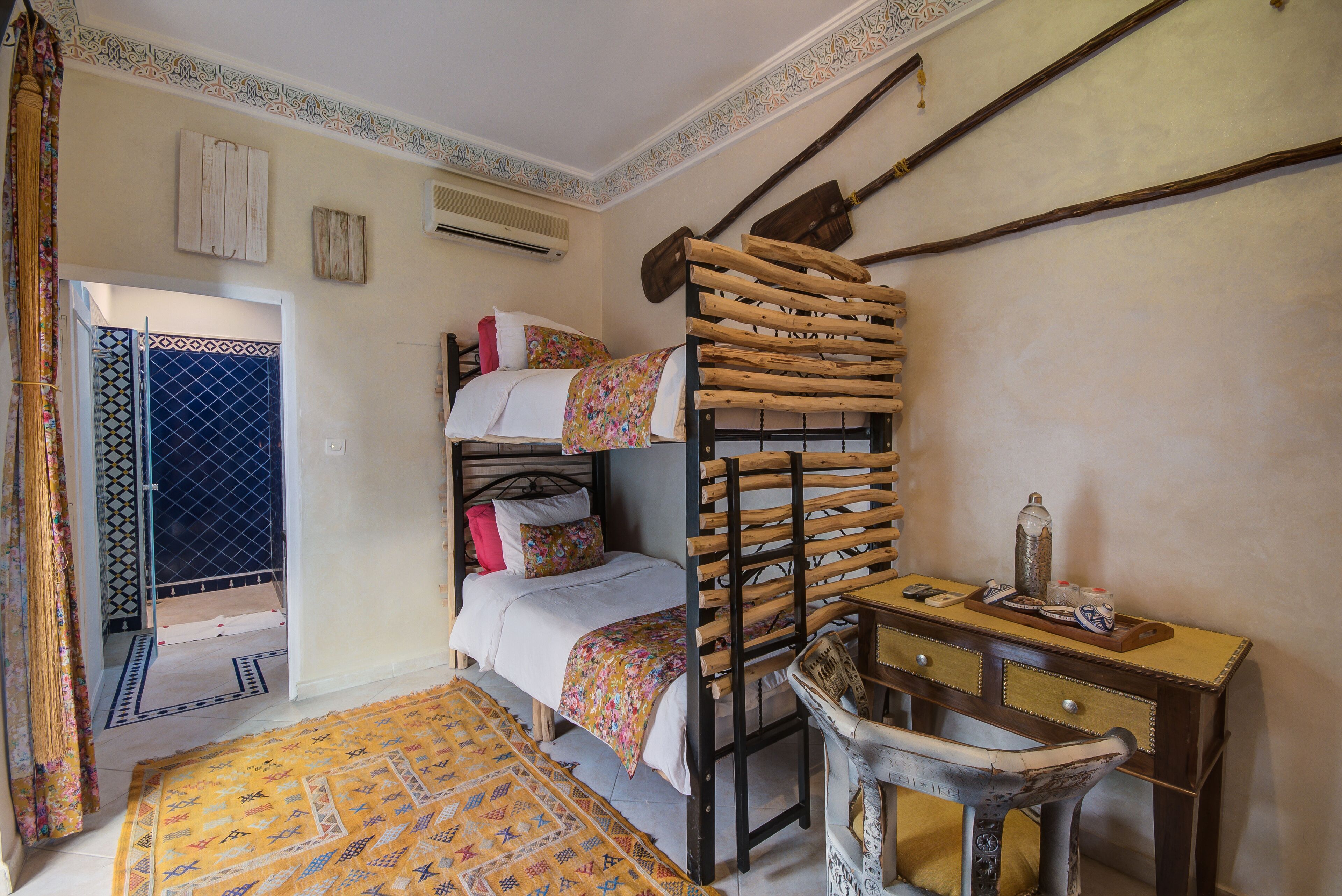 A room with a bunk bed, a desk with drawers, a chair, and a patterned rug.