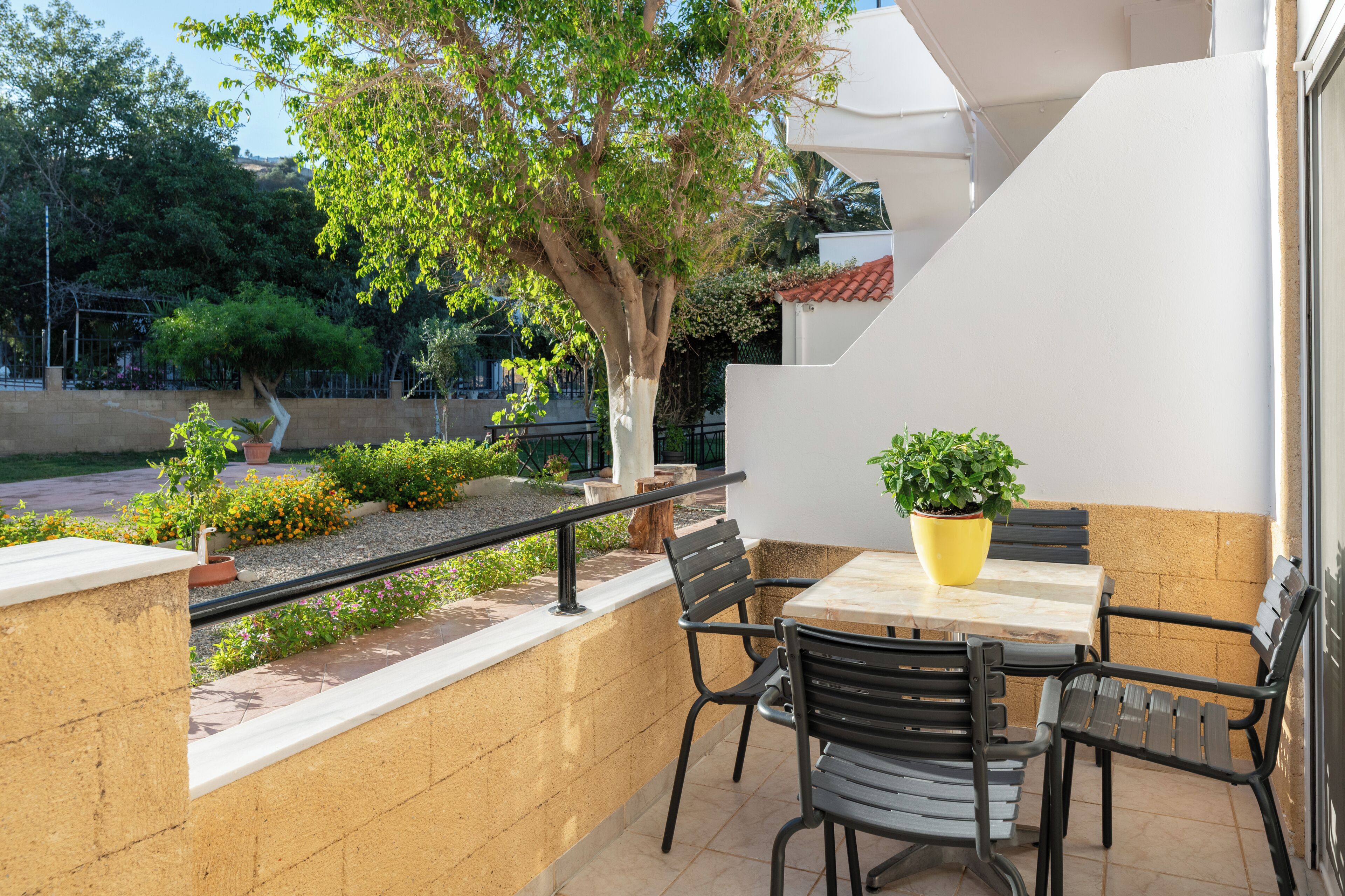 Un patio al aire libre con una mesa y sillas, rodeado de plantas y vistas a la calle.