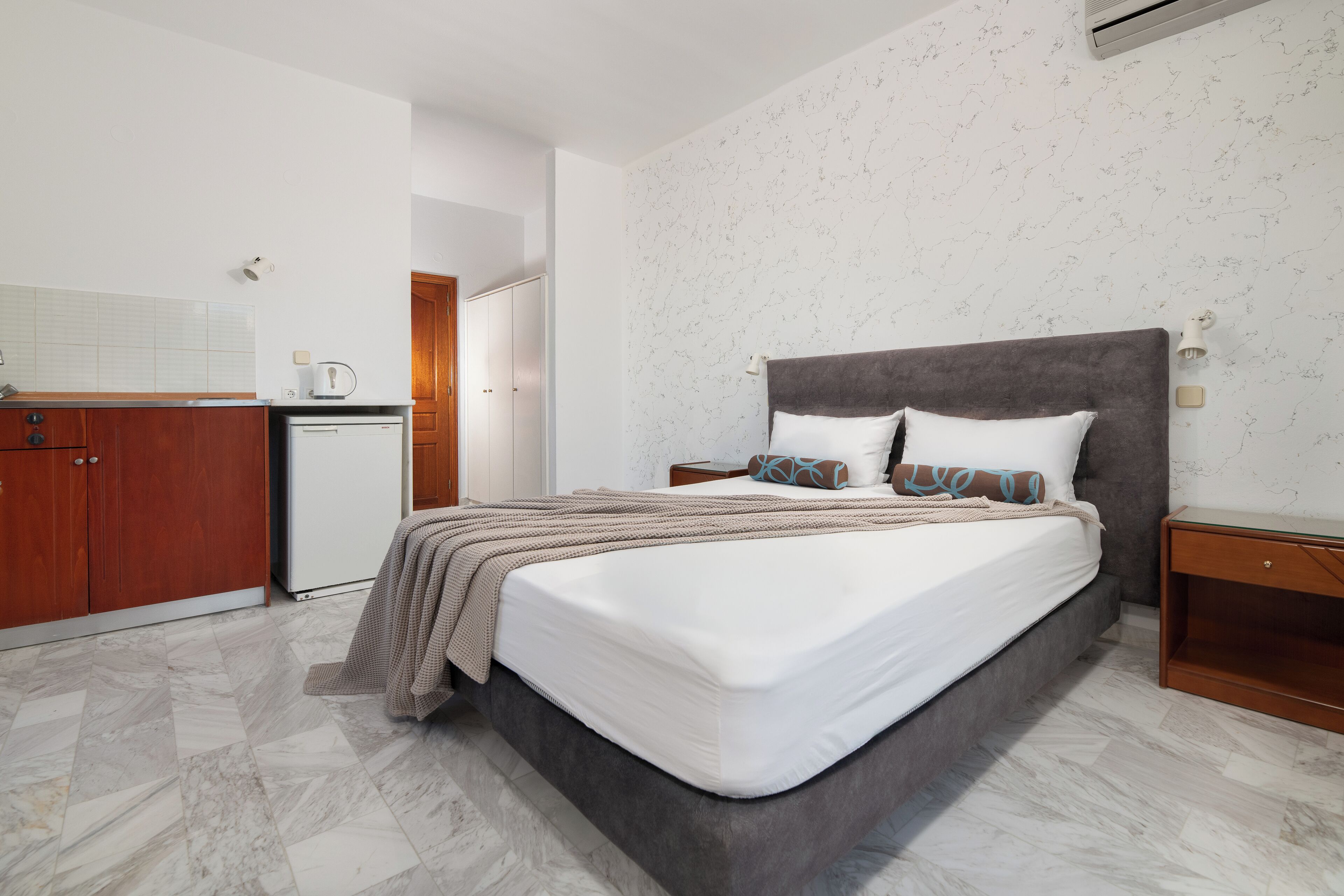 Une chambre avec un lit, des tables de chevet, une armoire et un coin cuisine.