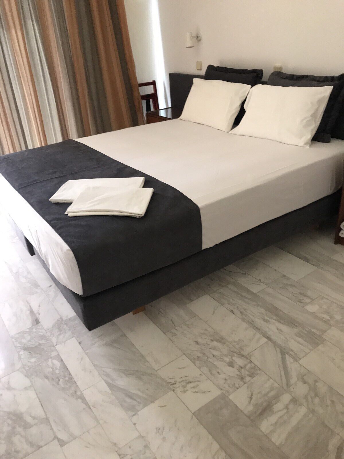 A neatly made bed with a dark headboard, white bedding, and a folded white towel on the bed.