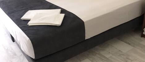 A neatly made bed with a dark headboard, white bedding, and a folded white towel on the bed.