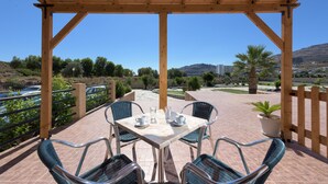 An outdoor patio with a wooden pergola, a table set with chairs, and a view of a mountainous landscape. - Vlycha Beach Studios & Apartments (Rhodes)