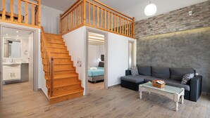 A modern interior with a wooden staircase, a sofa, a coffee table, and a brick wall. - Vlycha Beach Studios & Apartments (Rhodes)