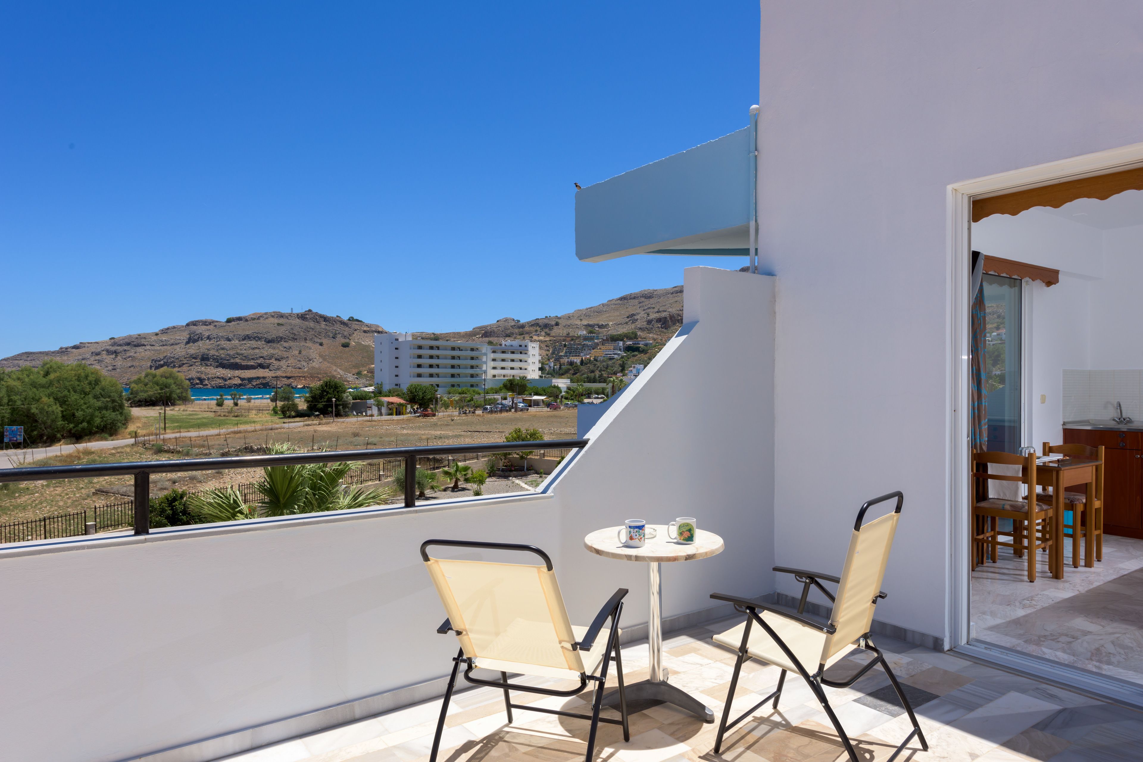A balcony with two chairs and a small table, overlooking a hillside with buildings.