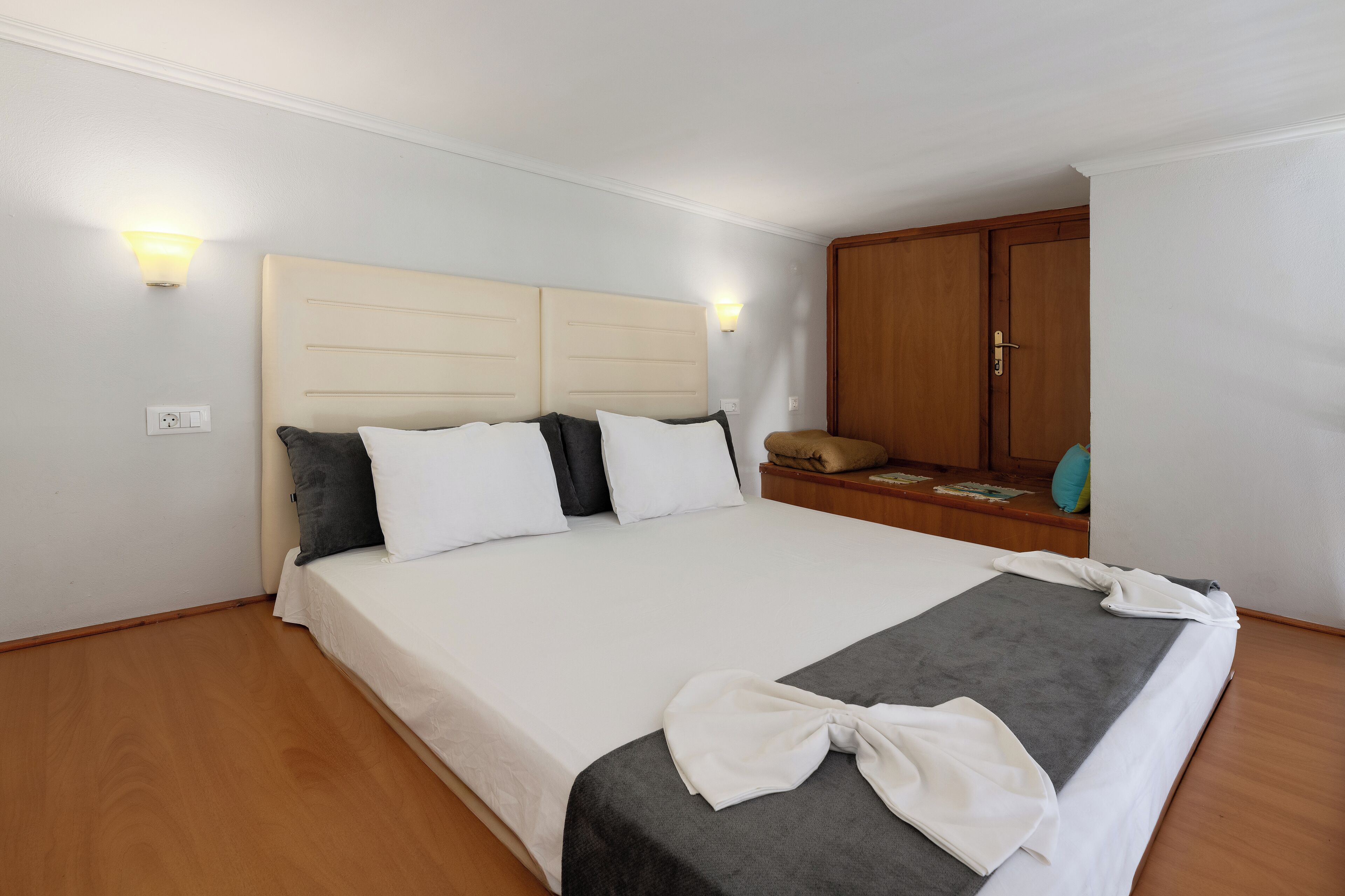 Una habitación de hotel con cama, lámparas de noche, armario y suelo de madera.
