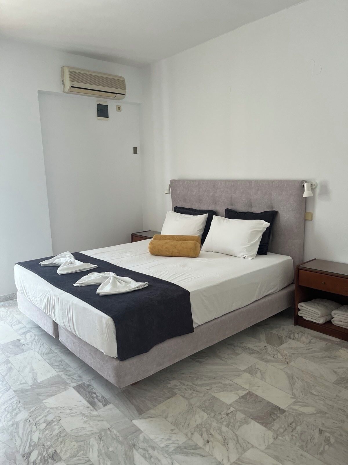 A neatly made bed with a grey headboard, white and black pillows, and a dark blue throw blanket.