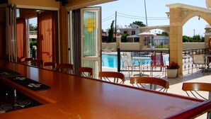 A bar area with a pool view, wooden chairs, and a poolside table. - Antonios Hotel (Rhodes)