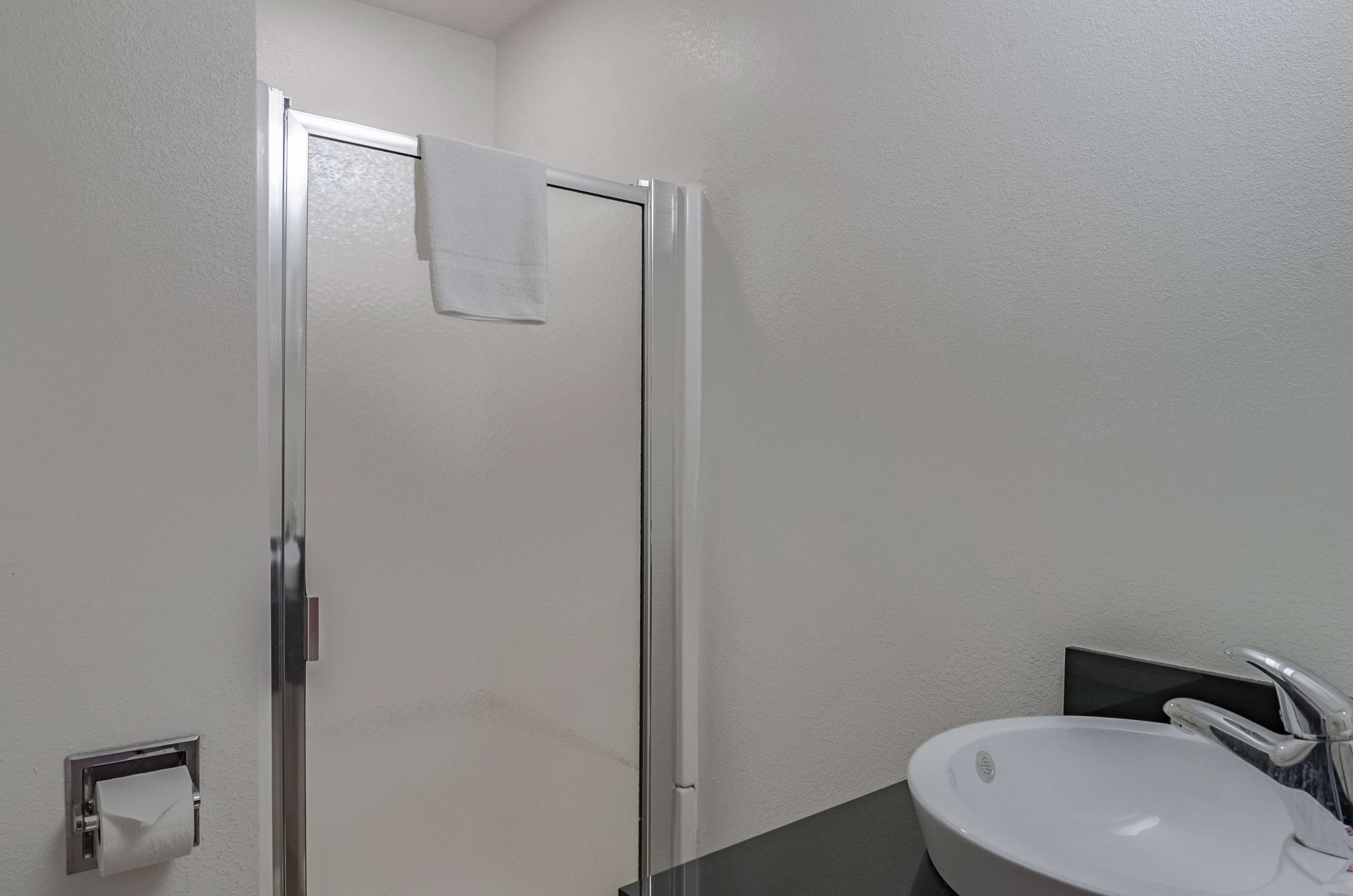 Ein Badezimmer mit Duschabtür aus Glas, einem weißen Waschbecken und einem Handtuch, das an der Tür hängt.