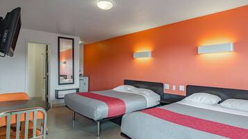 A hotel room with two beds, a TV, a desk, and a mirror.