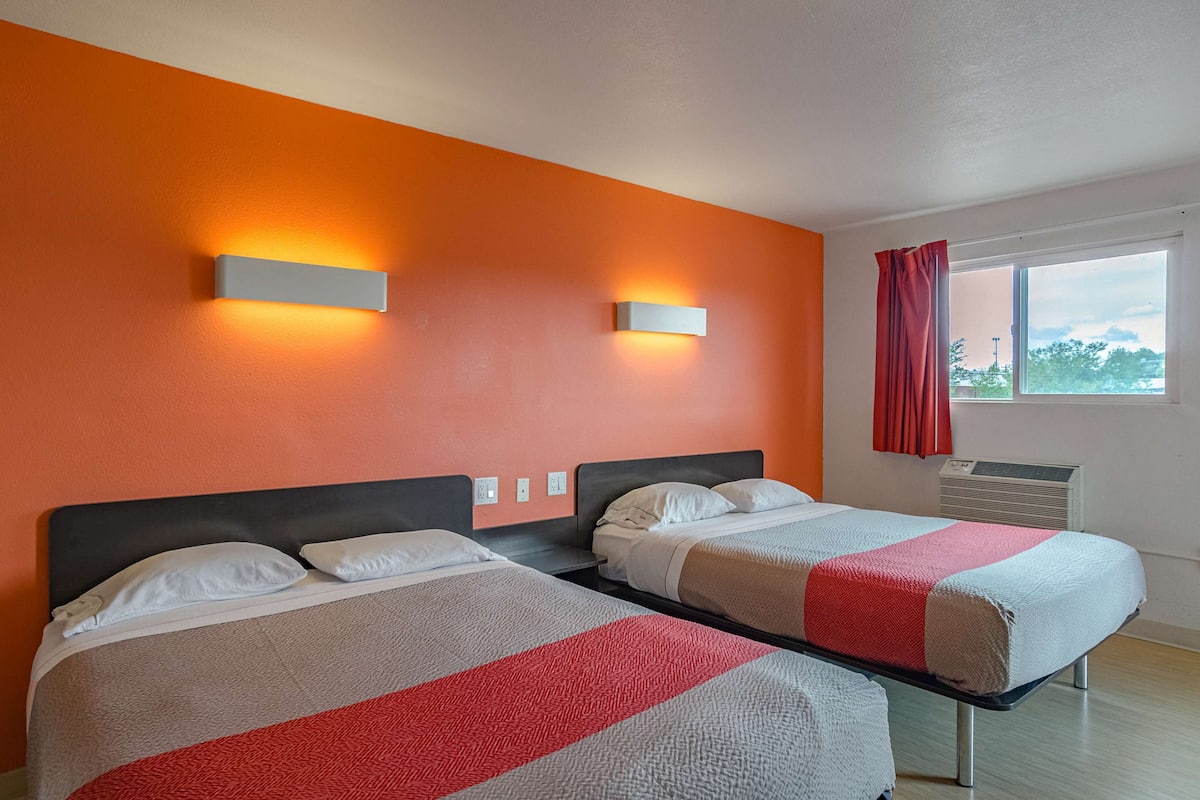 Ein Hotelzimmer mit zwei Betten, orangen Wänden und einem Fenster mit roten Vorhängen.