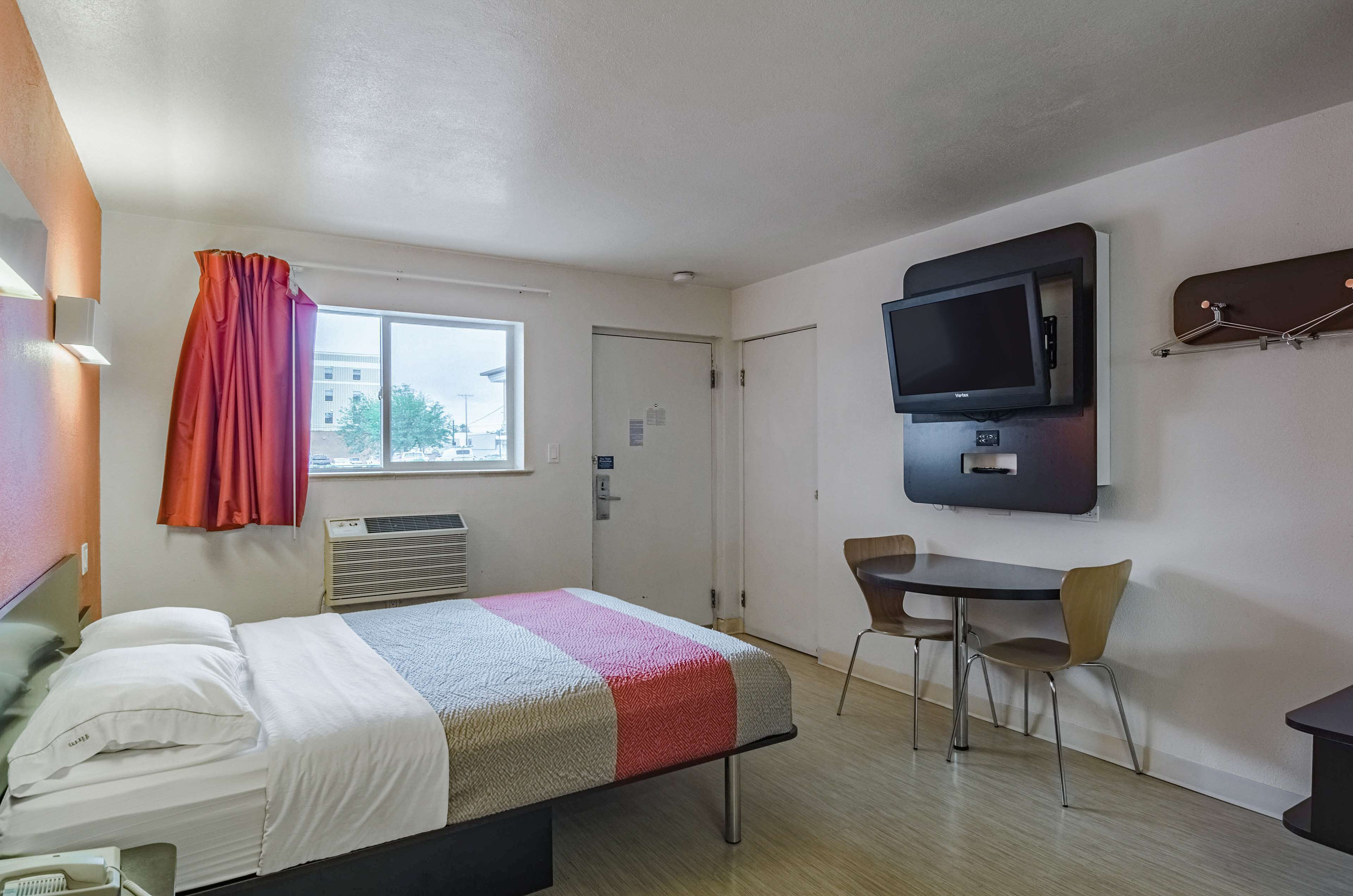 Habitación de hotel con cama, televisión montada en la pared, escritorio con silla y ventana con cortinas.
