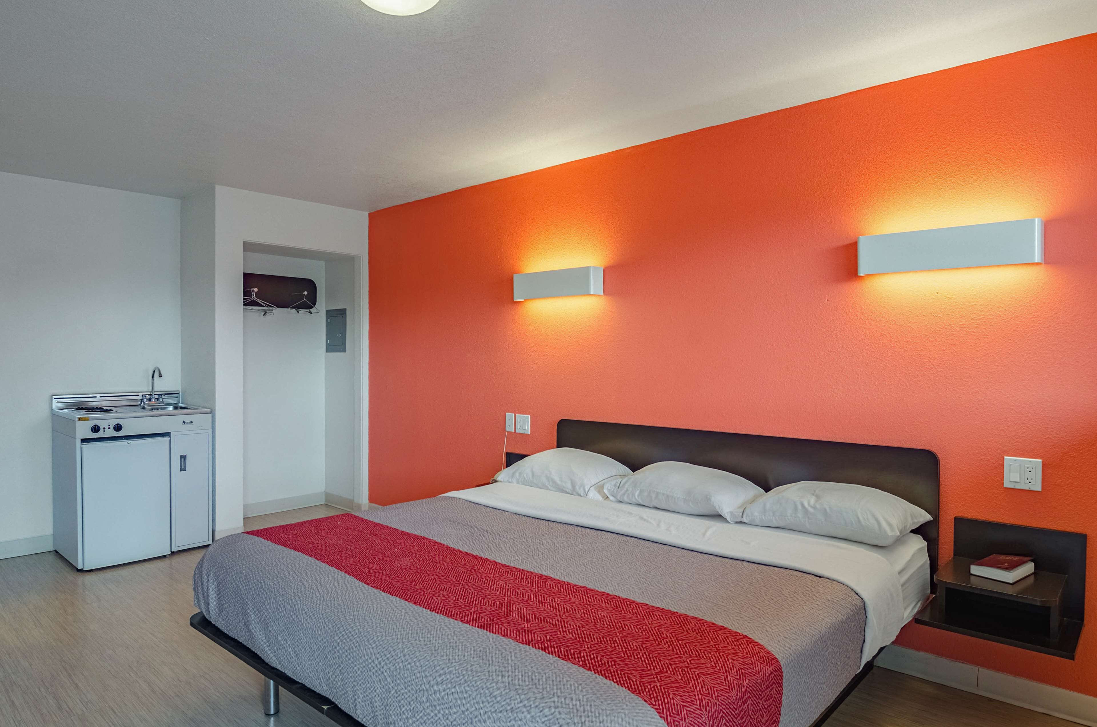A hotel room with a bed, a small kitchenette, and a red accent wall.