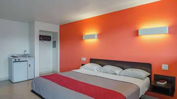 A hotel room with a bed, a small kitchenette, and a red accent wall.