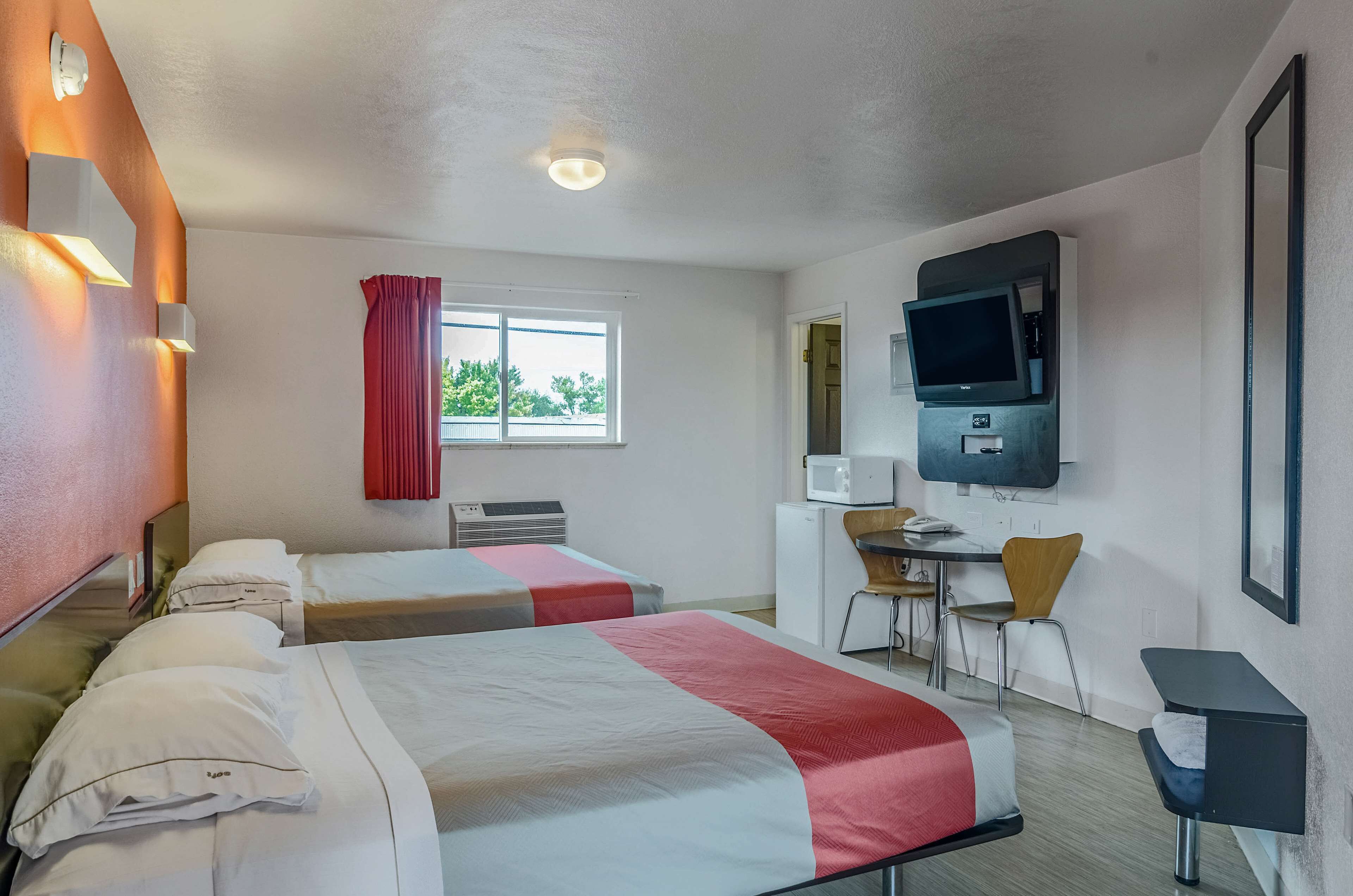 A hotel room with two beds, a desk with a chair, a television, and a window with curtains.