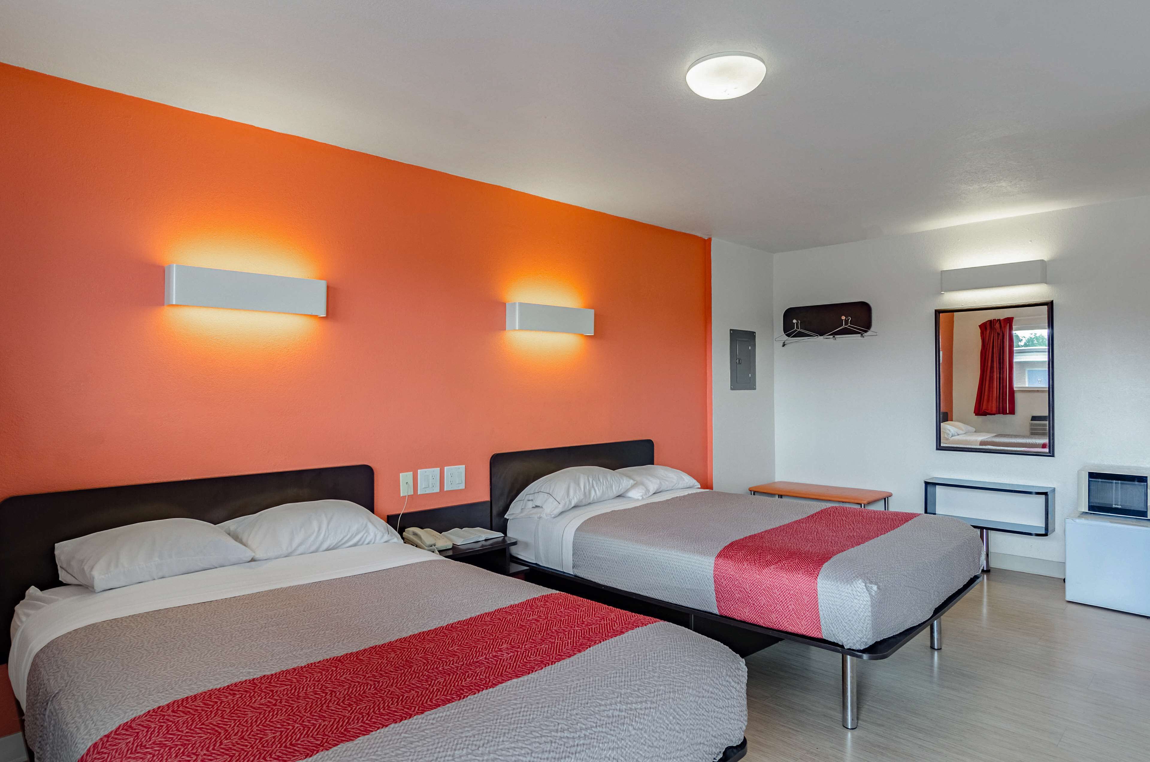 A hotel room with two beds, a desk, a chair, a TV, and a mirror.