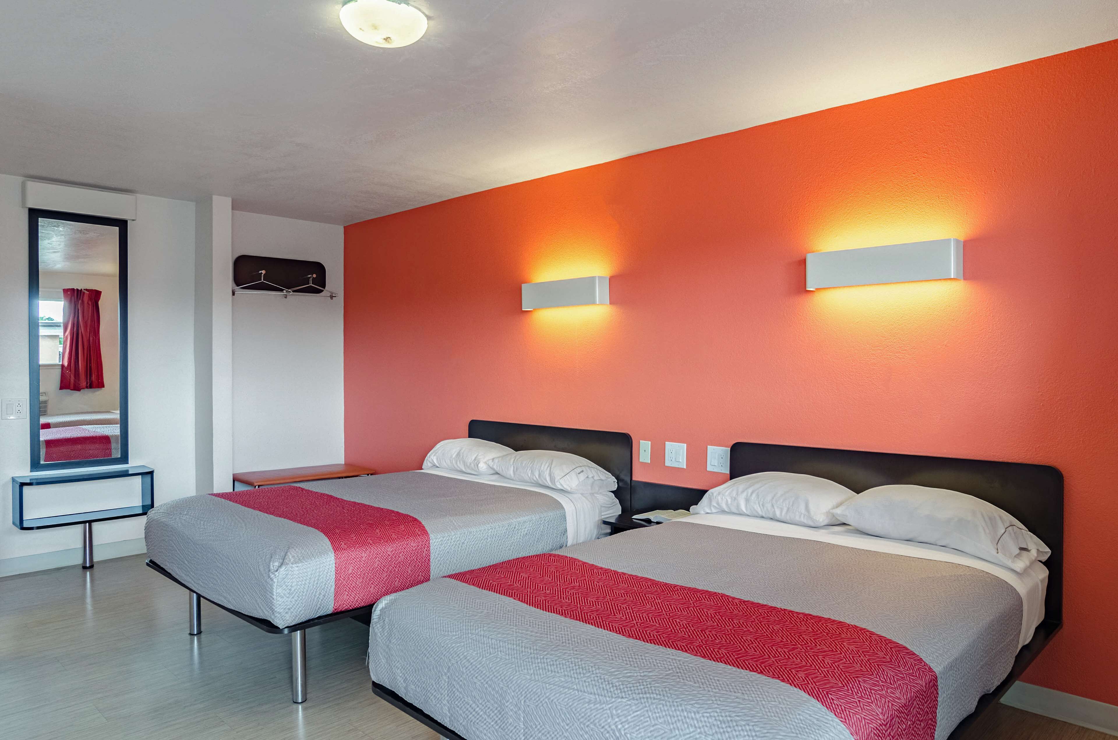 A hotel room with two beds, a red wall, and a mirror with a red curtain.