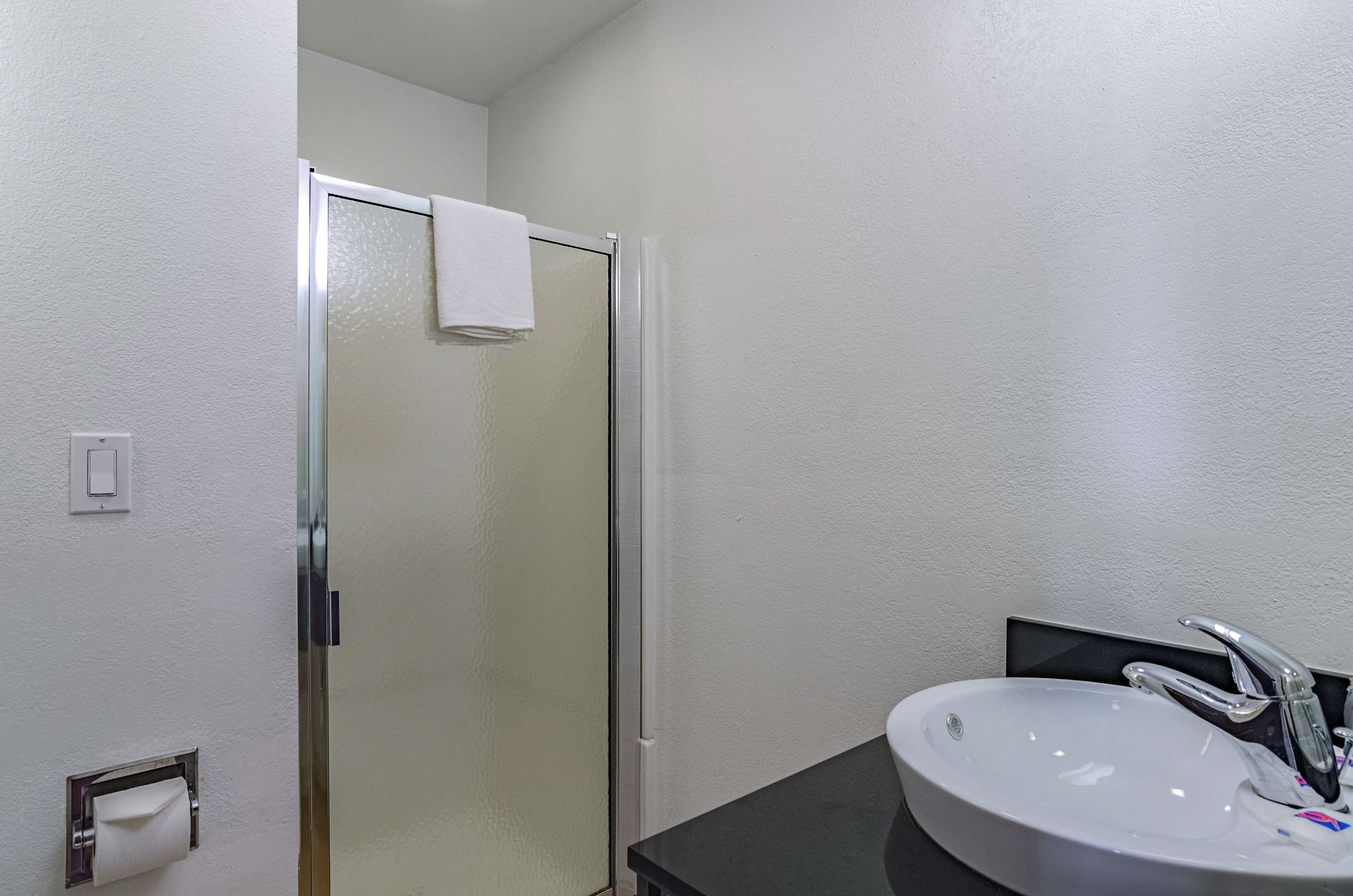 A bathroom with a glass shower door, a white sink with a modern faucet, and a towel hanging on the shower door.