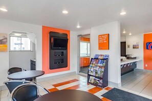 A modern hotel lobby with a reception desk, seating area, and a large TV screen. - Motel 6 Riverton, WY (Riverton)
