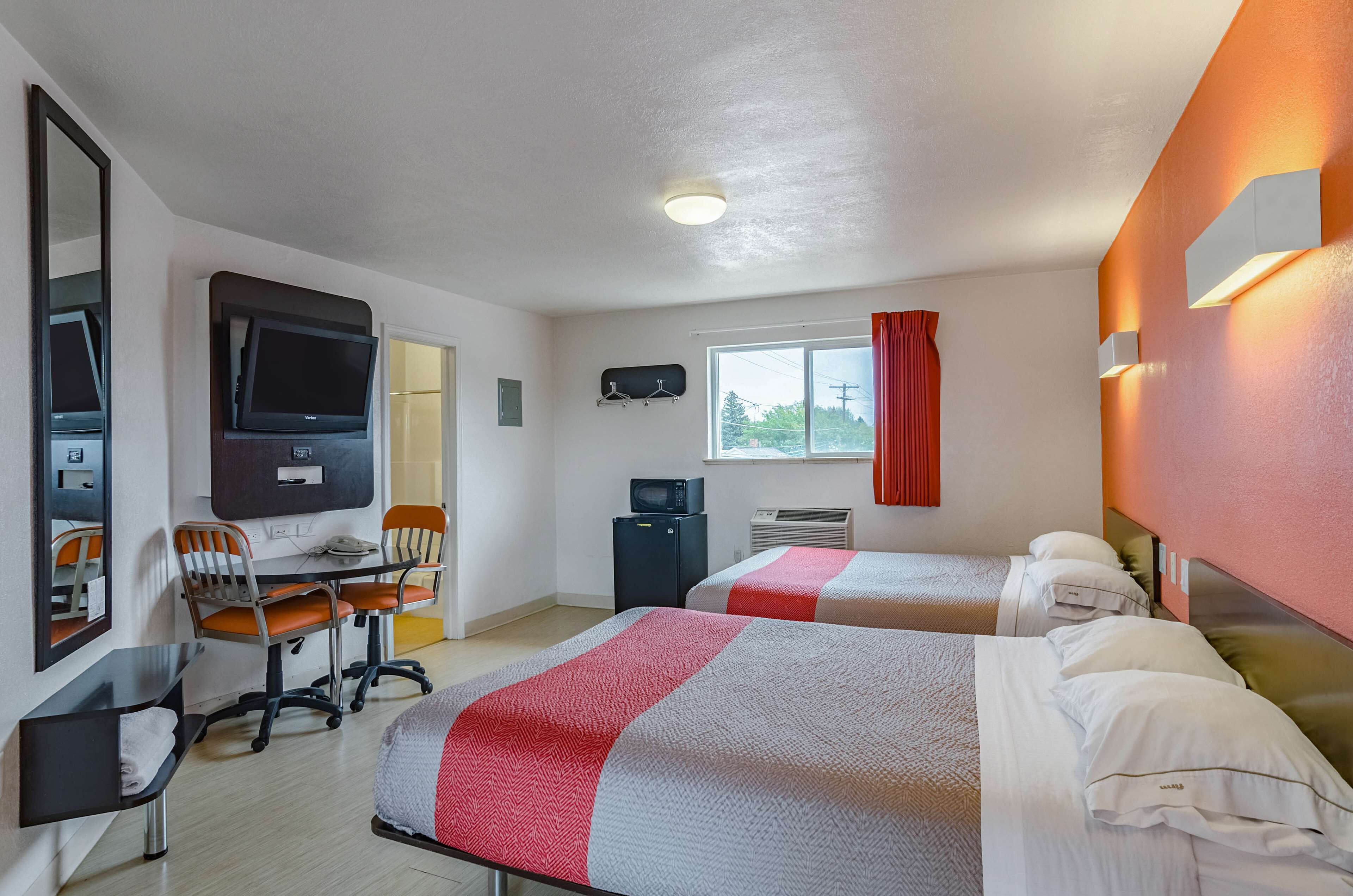 A hotel room with two beds, a desk with a chair, a TV, and a window with curtains.