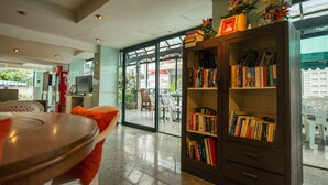 A library with bookshelves, a table with a chair, and a view through glass doors to an outdoor area.