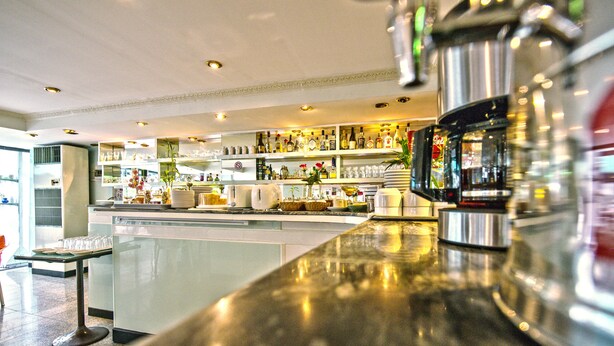 A bar area with a polished counter, shelves with bottles, and a decorative vase.