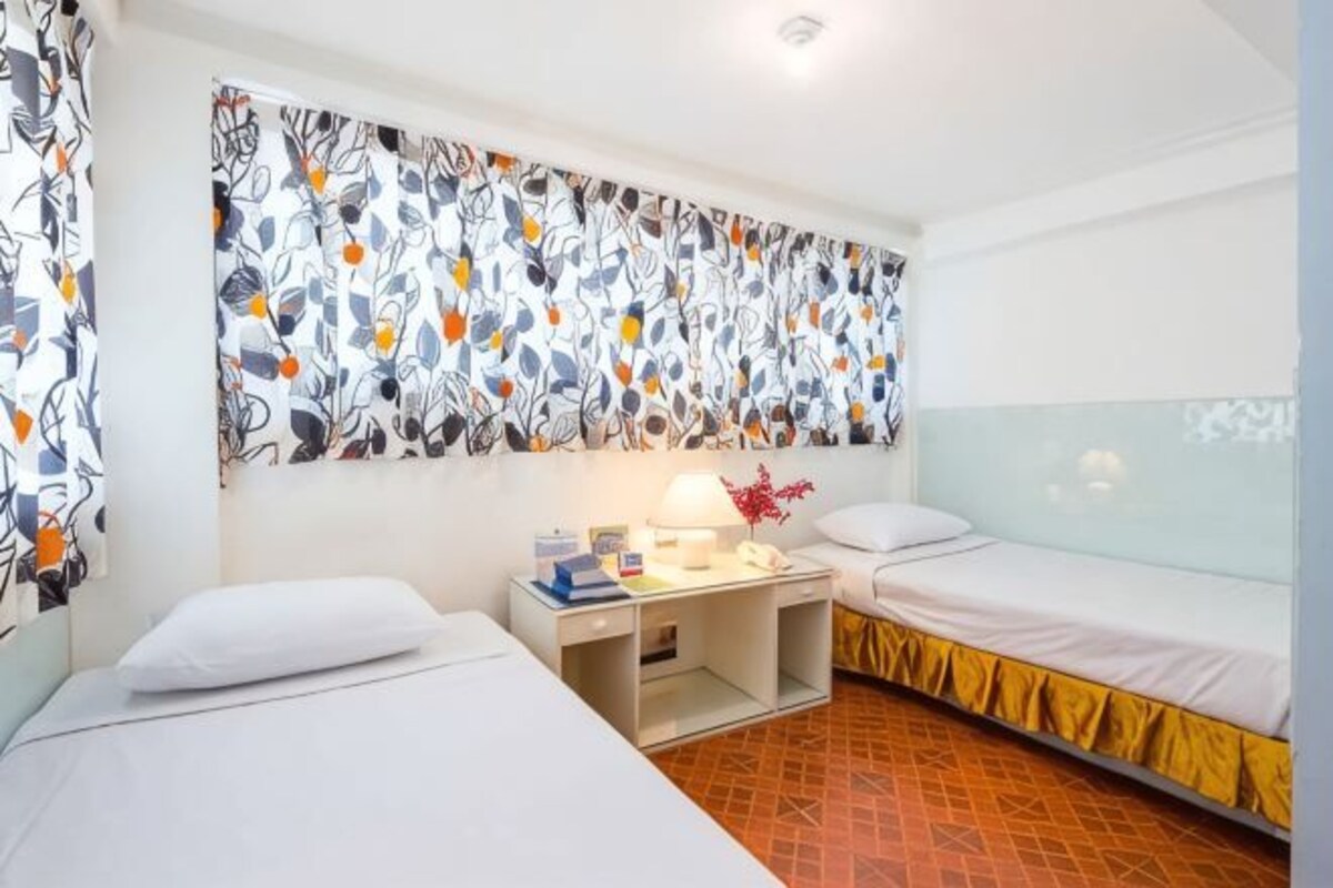 A hotel room with two beds, a desk with a lamp, and a patterned curtain.