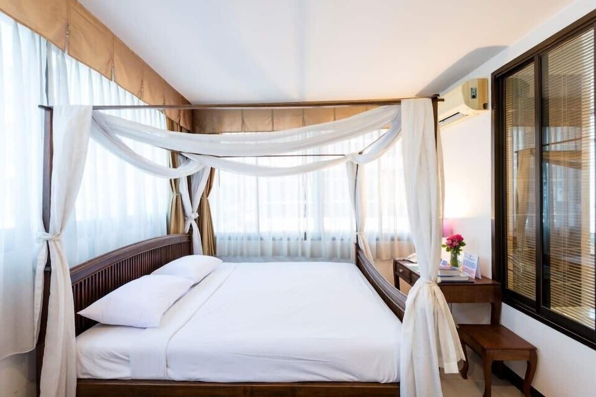 A bedroom with a canopy bed, a wooden headboard, a bedside table with a lamp, and a window with blinds.
