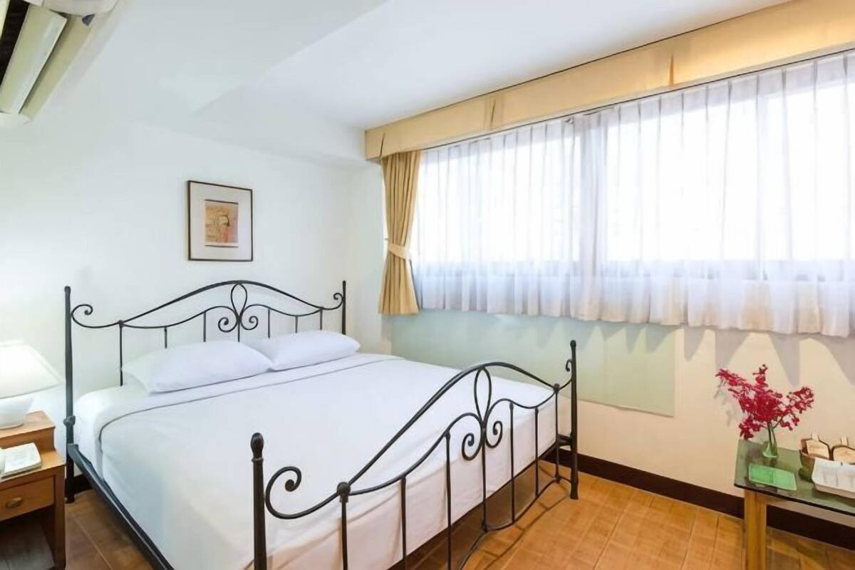 A bedroom with a bed, a nightstand, a window with curtains, and a small table with a vase.