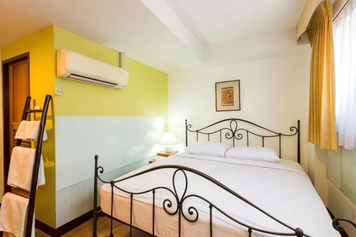 A room with a bed, a wall-mounted air conditioner, a bedside lamp, and a framed picture on the wall.