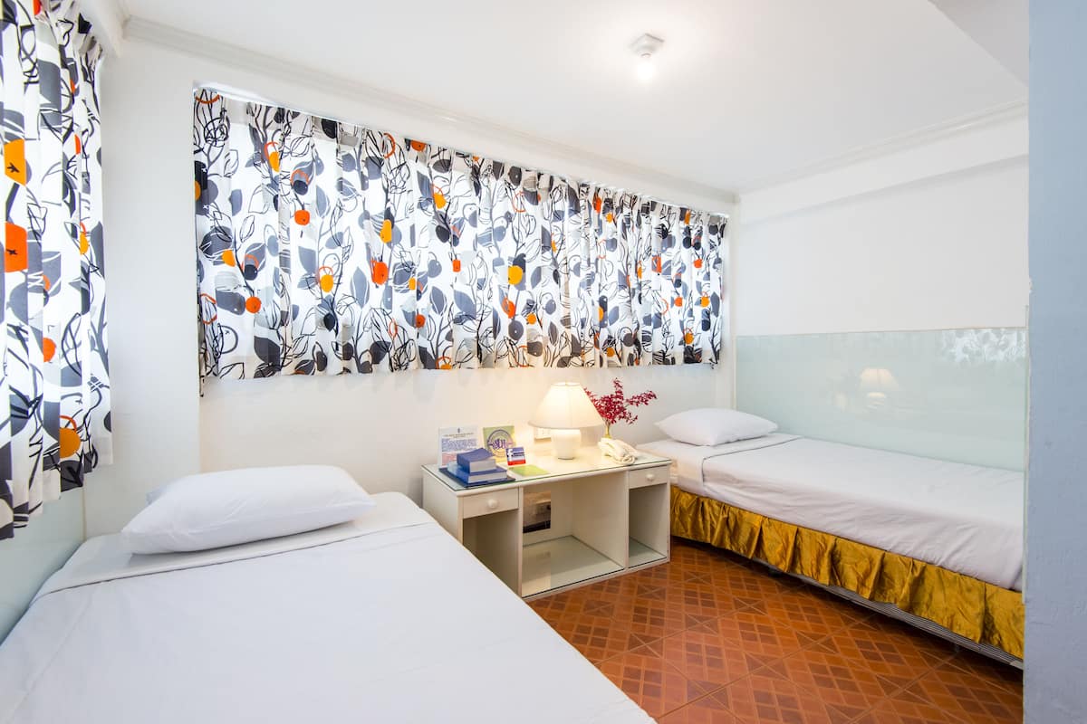 A hotel room with two beds, a nightstand with a lamp, and a patterned curtain.