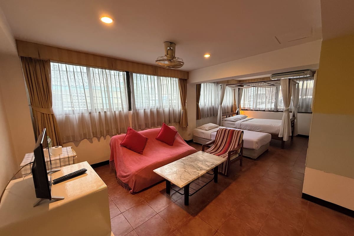 A hotel room with a sofa, a small table, a bed with a canopy, and a TV.