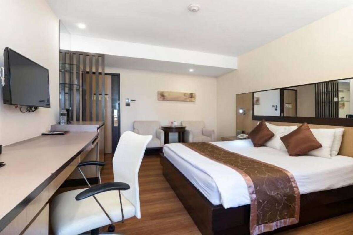 A hotel room with a bed, a desk, a chair, a small table, and a TV.