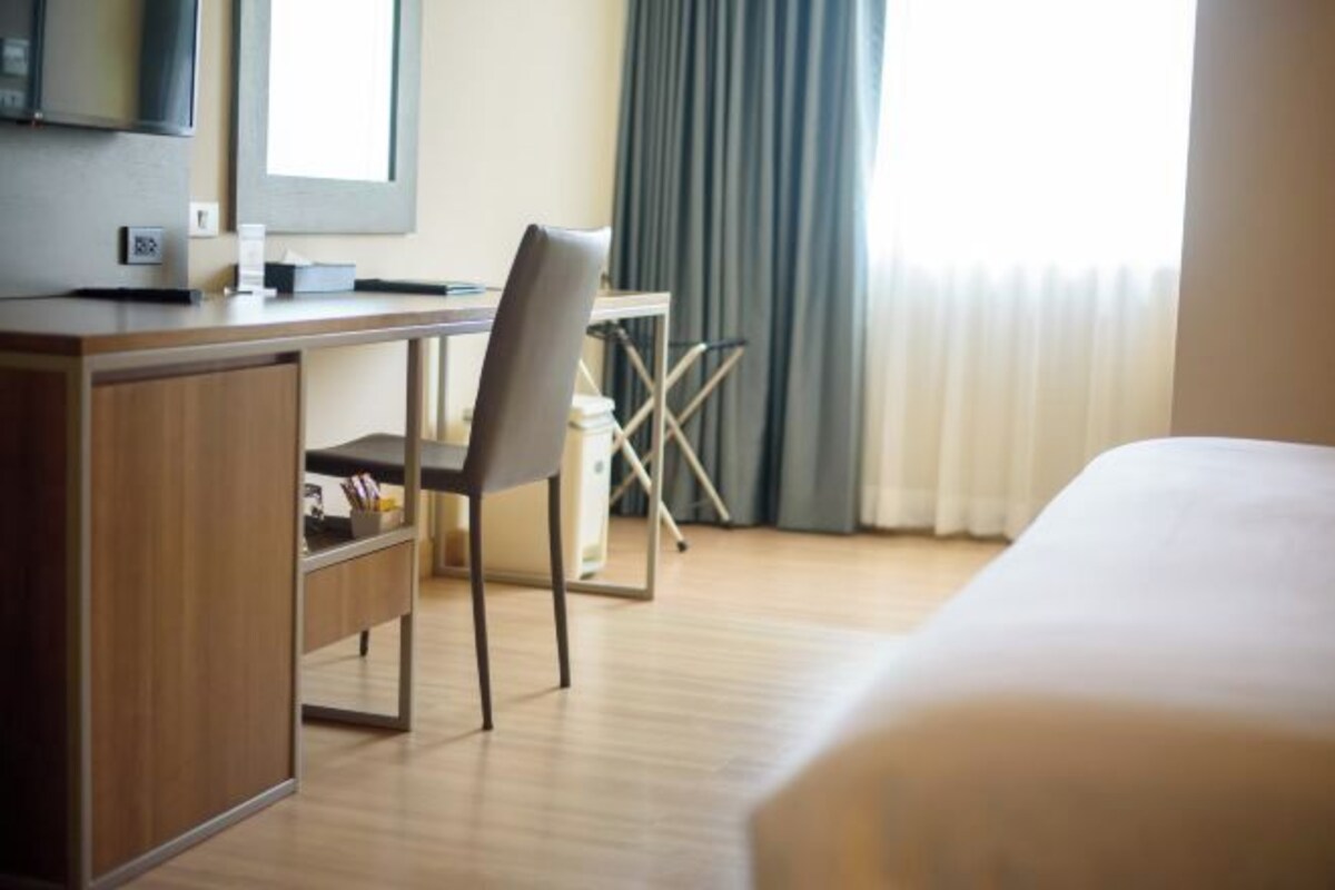 A hotel room with a bed, a desk with a chair, a television, and a window with curtains.