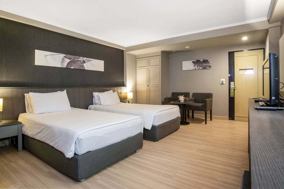 A hotel room with two beds, a desk, a chair, and a TV.