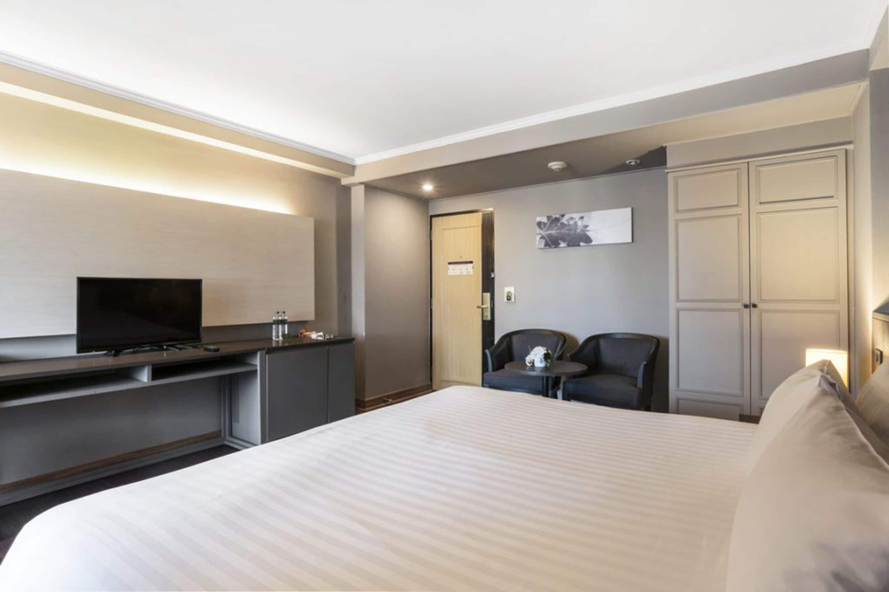 A hotel room with a bed, a TV, a desk, a chair, and a wardrobe.