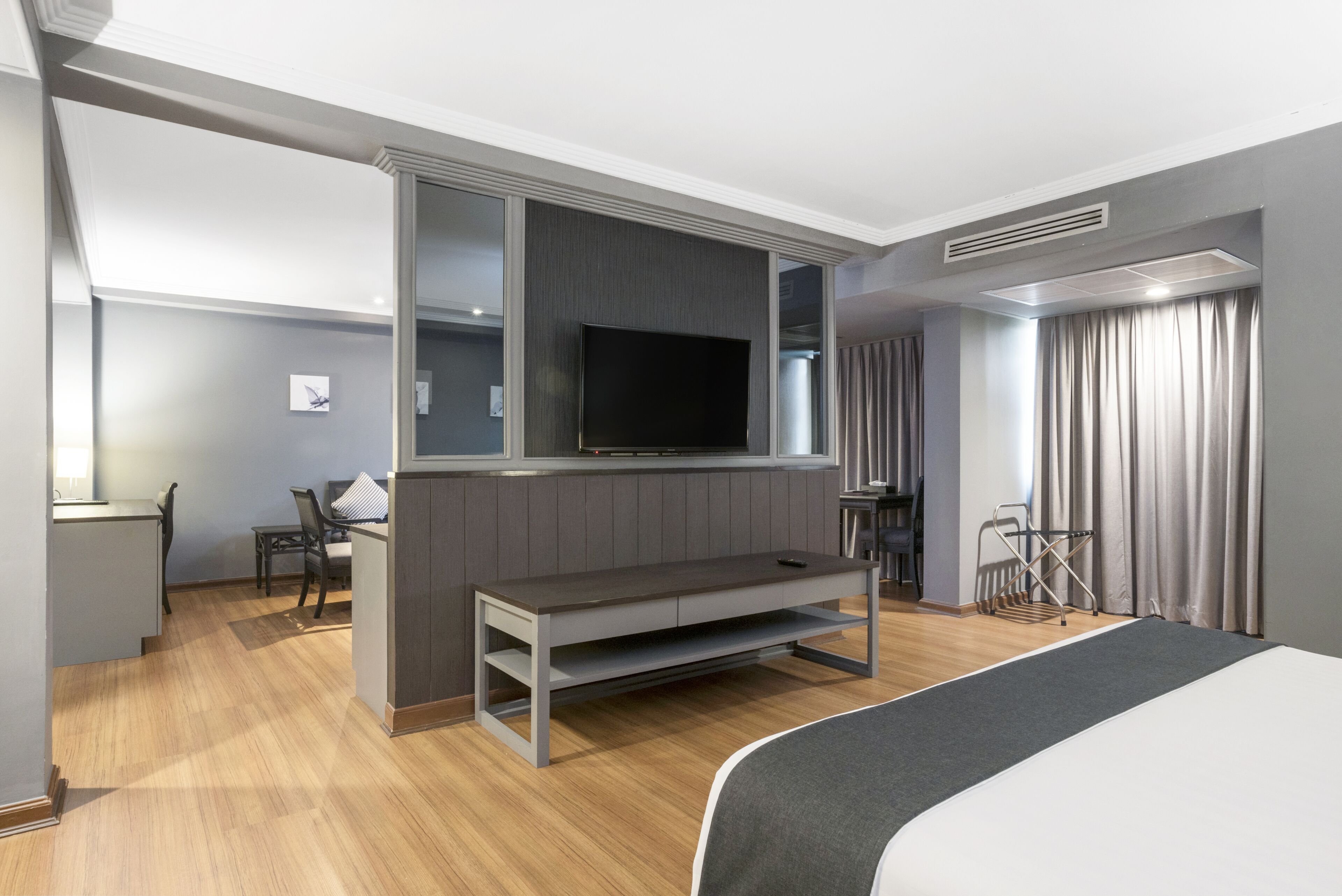 Habitació d'hotel moderna amb un llit gran, un televisió de pantalla plana penjada a la paret, una zona de seients petita amb taula i cadires, i una finestra amb cortines.