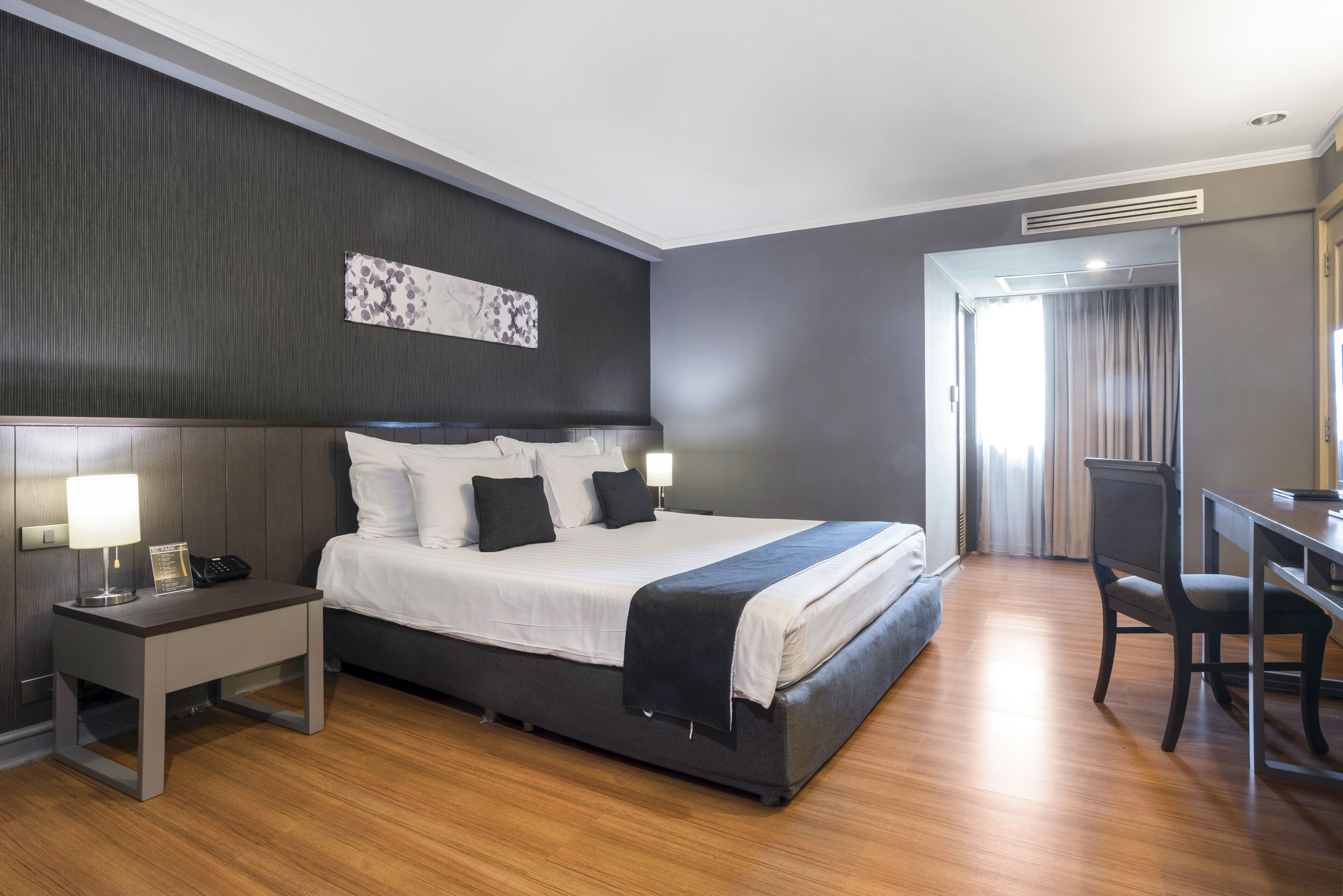 A modern hotel room with a large bed, bedside tables, a desk, and a chair.